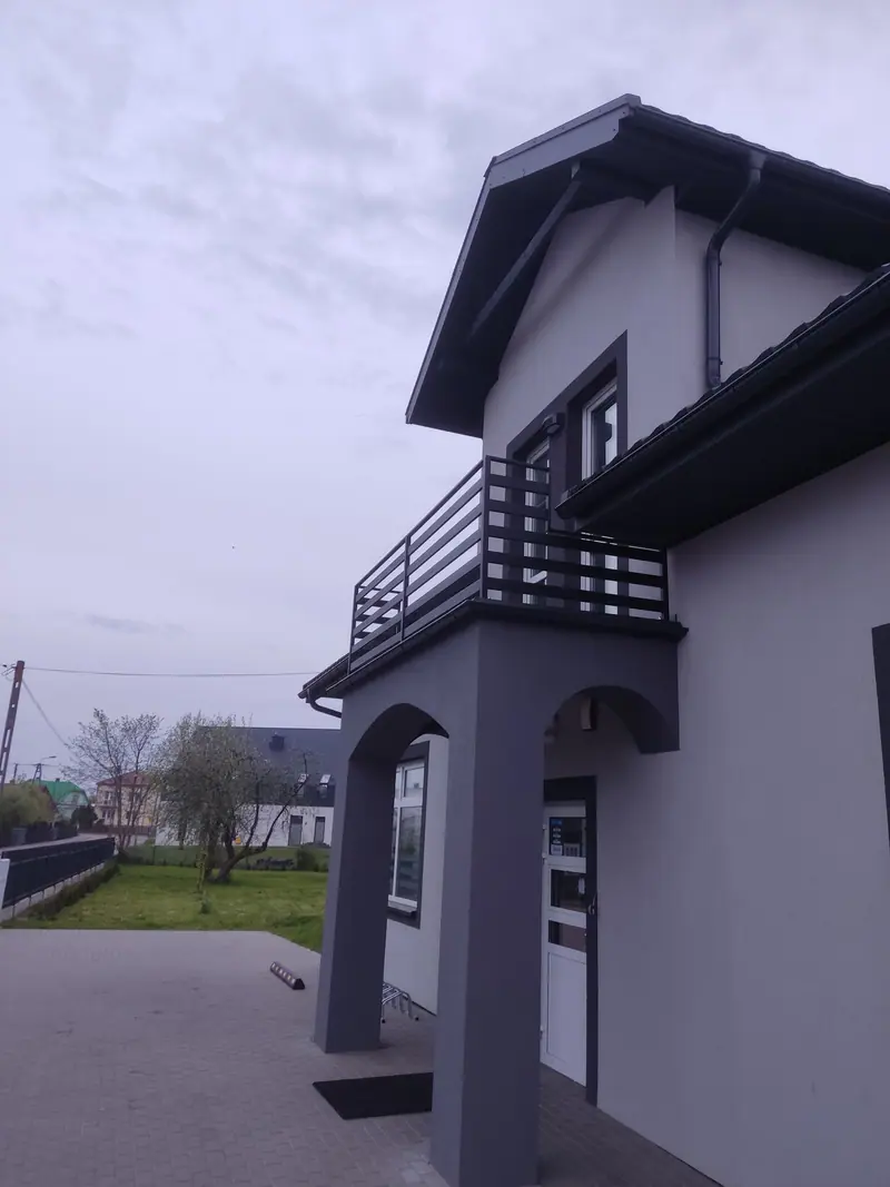 Balkon z balustradą z poziomych profili nad łukowym zadaszeniem wejścia