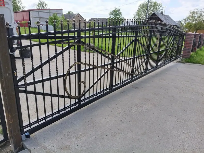 Brama przesuwna ze skręcanych prętów stalowych ze spiralnym ornamentem, między słupkami z cegły