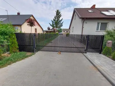 Brama przesuwna z pionowych profili stalowych zamykająca podjazd z kostki brukowej