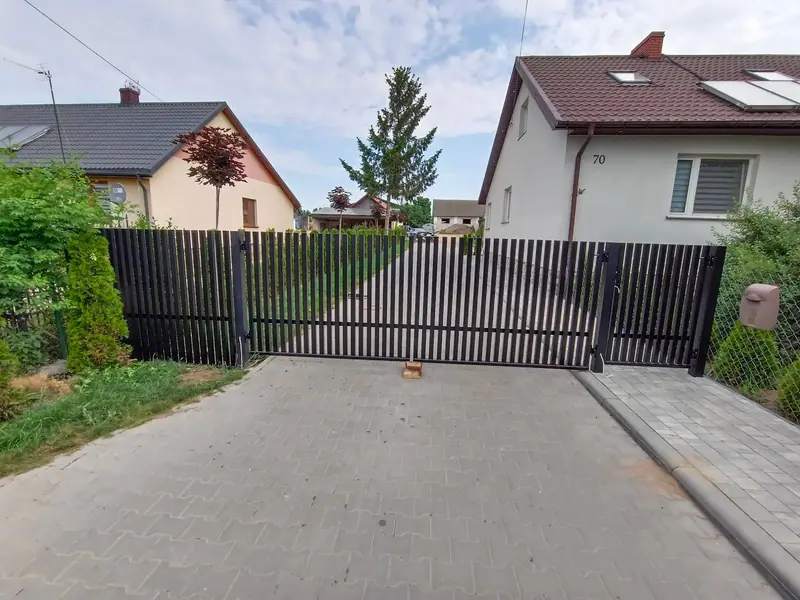Brama przesuwna z pionowych profili stalowych zamykająca podjazd z kostki brukowej