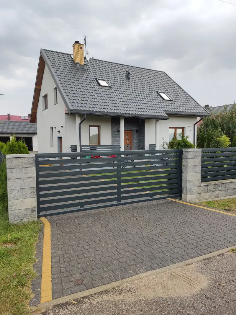Brama skrzydłowa z poziomych profili i przęsła ogrodzenia w tym samym wzorze przed domem jednorodzinnym