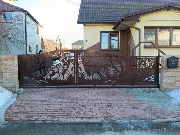 Brama skrzydłowa z blachy stalowej z ażurowym wzorem jeleni i drzew, zamykająca wjazd z kostki brukowej