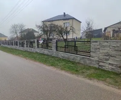 Przęsła ogrodzenia z geometrycznym wzorem na podmurówce z bloczków wzdłuż drogi
