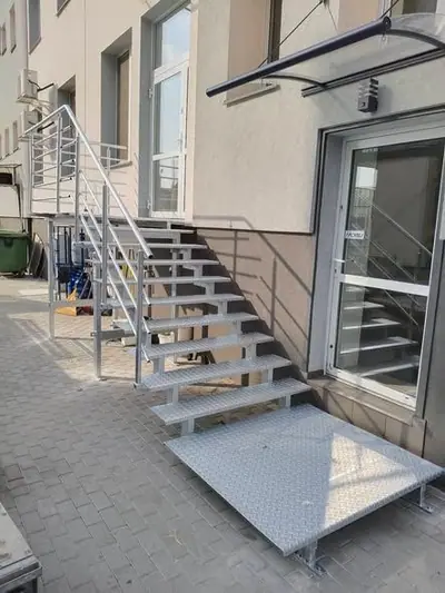 Stalowe schody zewnętrzne z podestem i balustradą z rur przy wejściu do budynku